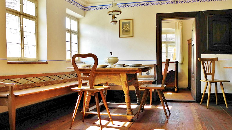 Innenansicht geräumige Stube mit gedecktem Tisch und Holzstühlen